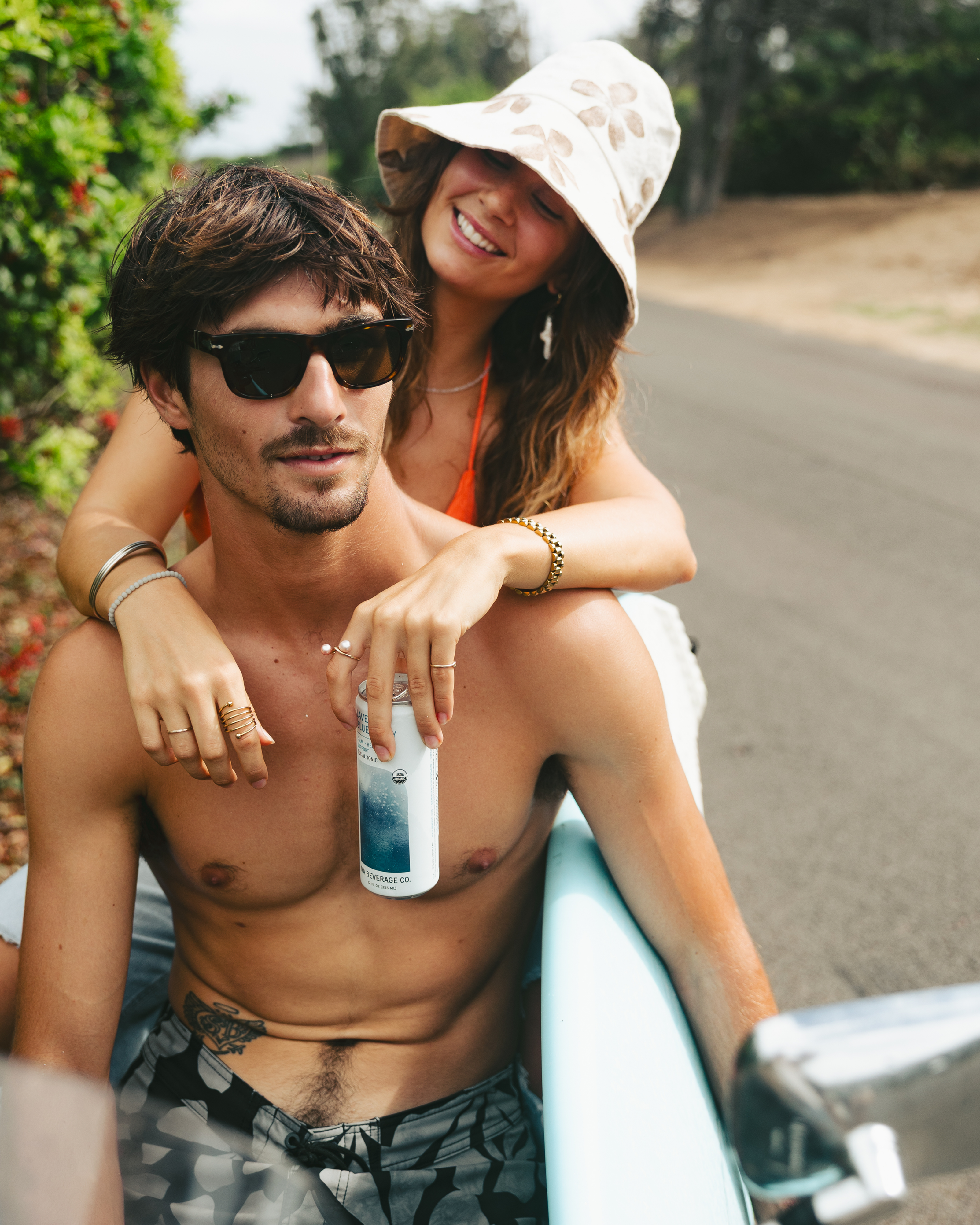 Man and woman sitting on a moped with a can of NA, outdoors.